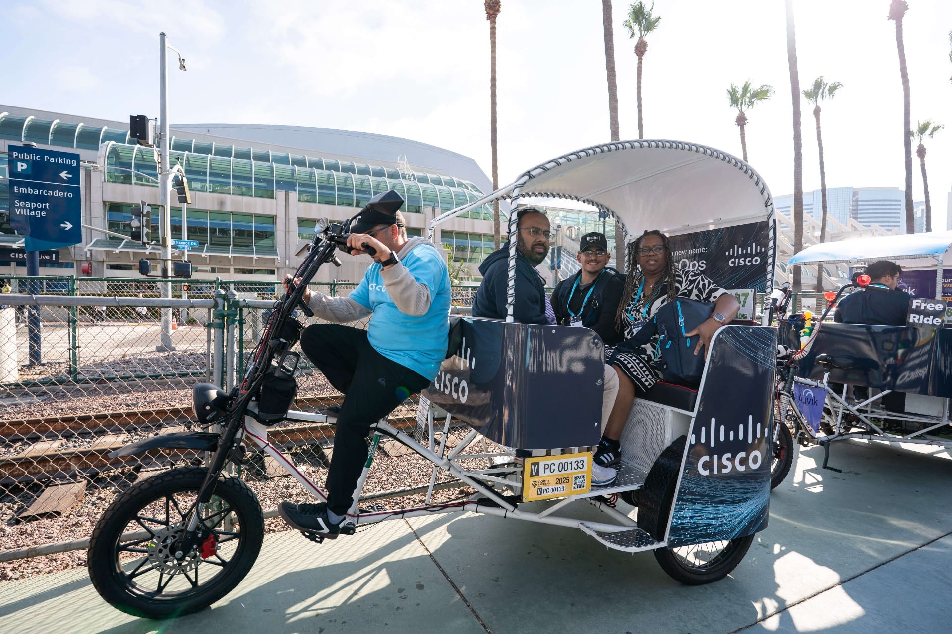 Cisco pedicab passengers smiling at a Convention Center crossing in San Diego