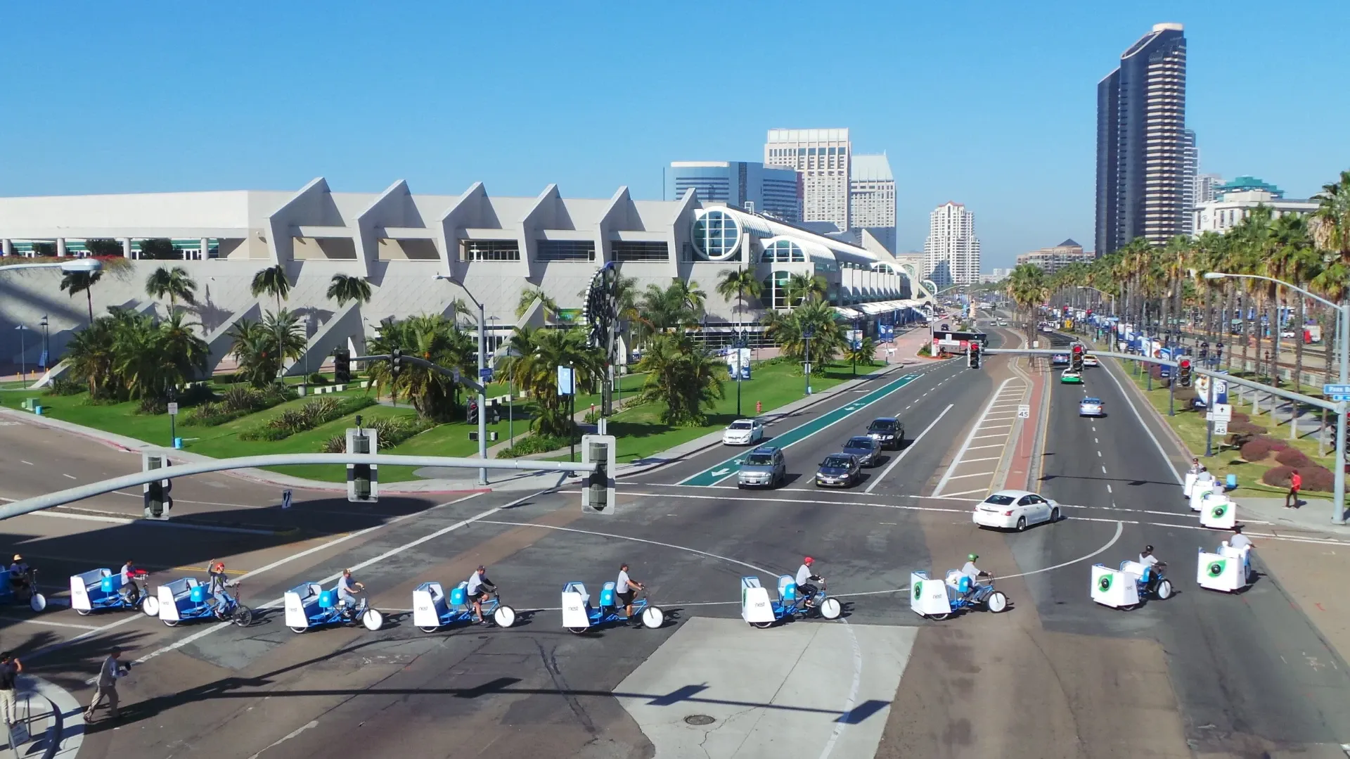Aerial view of a branded pedicab fleet riding past the San Diego Convention Center with the downtown skyline
